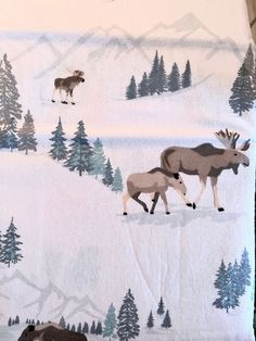 two animals are walking in the snow with trees and mountains behind them on a blanket