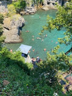 people are swimming in the clear blue water near some rocks and trees, surrounded by greenery