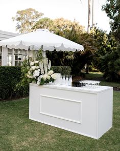 an outdoor bar with white flowers and wine glasses on the counter, under an umbrella