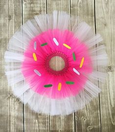 a pink and white tutu with sprinkles on it sitting on top of a wooden floor