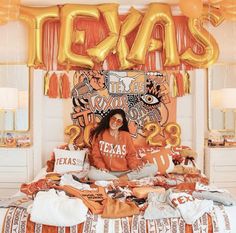 a woman sitting on top of a bed in front of balloons and letters that spell out texas