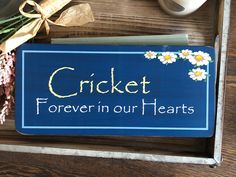 a blue sign that says cricket forever in our hearts on it next to flowers and a cup