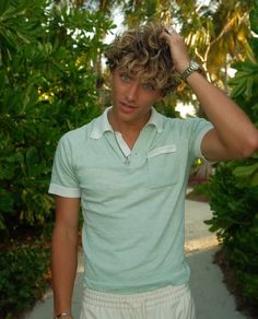 a young man is holding his hair in the air while standing on a path surrounded by trees