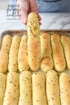 someone is holding a piece of bread in the middle of a baking pan filled with garlic breadsticks