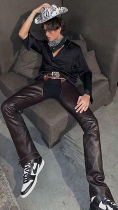 a man sitting on top of a couch wearing leather pants and a silver metal hat