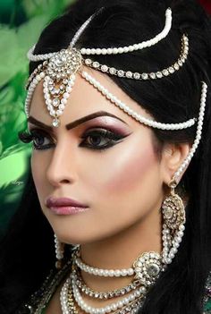 a woman with long black hair wearing a headpiece and pearls on her face,