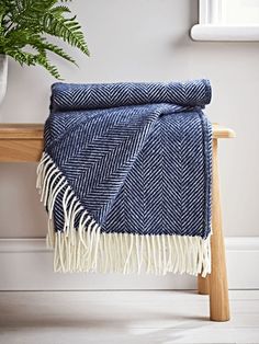 a blue and white blanket sitting on top of a wooden bench next to a potted plant