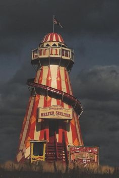 a large red and white striped tower on top of a hill under a cloudy sky