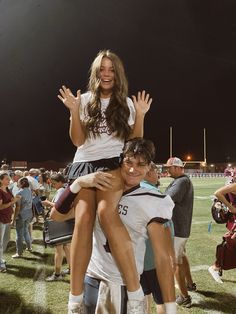 two young people are hugging on the football field at night with fans in the background