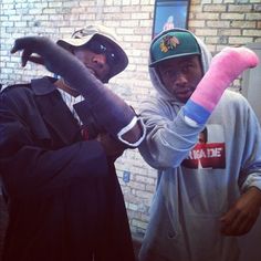 two young men standing next to each other in front of a brick wall holding something pink