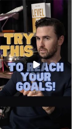 a man in a black shirt is holding a microphone and looking at the camera with text that reads try this to reach your goals