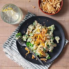 a black plate topped with pasta and broccoli next to a glass of milk