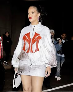 a woman in white jacket and skirt with red paint on her body walking down the street