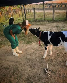 a woman in green jumpsuits feeding a black and white cow