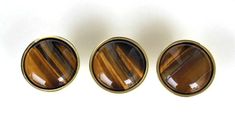 three brown and black glass cabochles on a white surface with gold rims