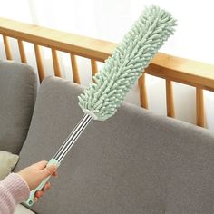 a person holding a dust mop on top of a couch