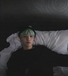 a young man with green hair laying in bed