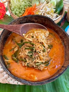 a wooden spoon in a bowl filled with soup and veggies on a table