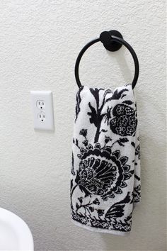 a black and white floral towel hanging on a wall next to a toilet paper dispenser