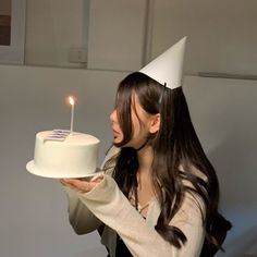 a woman in a party hat holding a cake with a lit candle on the top