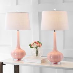 two pink vases with flowers in them sitting on a shelf next to a lamp