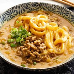 a bowl filled with noodles and meat on top of a black table next to chopsticks