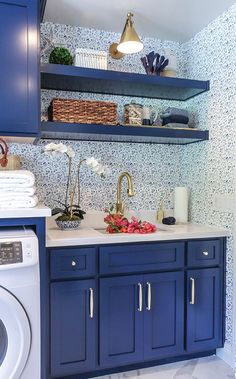 a washer and dryer in a small room with blue cabinets, white counter tops and floral wallpaper