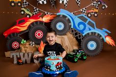 a young boy sitting in front of a birthday cake with monster trucks on the background