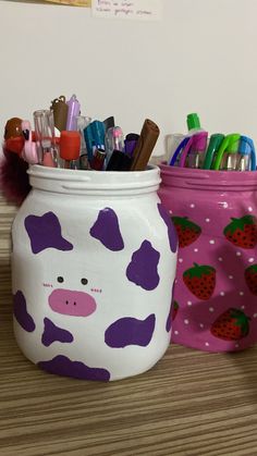 two jars with pens, markers and pencils in them sitting on a table next to each other