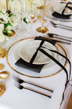 a table set with white and gold plates, black napkins, and silverware