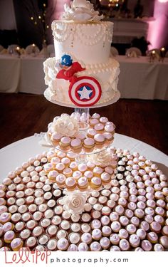 three tiered wedding cake with cupcakes and captain america topper on it