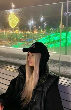 a woman with long blonde hair sitting on a bench wearing a black hat and jacket