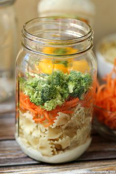 a mason jar filled with veggies and carrots on top of a wooden table