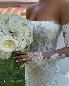 a woman in a wedding dress holding a bouquet of white flowers and lace gloves on her arm