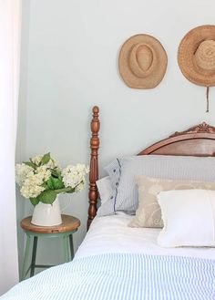 a bed with two hats on the headboard above it and flowers in vases