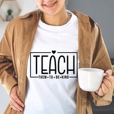 a woman holding a coffee cup and wearing a t - shirt that says teach them to be kind