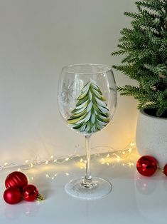 a wine glass with a christmas tree painted on it next to ornaments and a potted plant