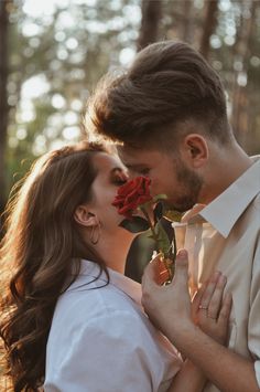 a man and woman kissing each other in the woods with red roses sticking out of their mouths