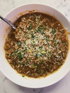 a white bowl filled with soup on top of a marble counter topped with parmesan cheese