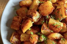 a white bowl filled with cooked potatoes on top of a wooden table