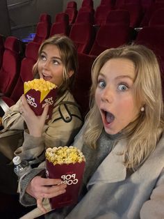 two women eating popcorn in an auditorium