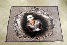 a man in a white hard hat is holding a drill and looking into a hole