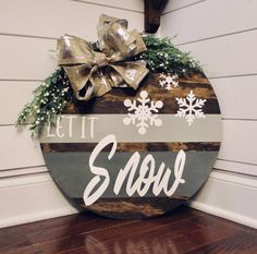 a wooden sign that says let it snow on the side of a house with christmas decorations