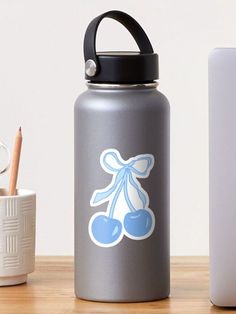 a silver water bottle with a blue bow and cherries sticker on it next to a cup