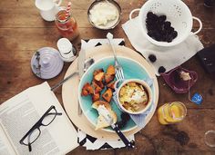 an open book on a wooden table with food and glasses, next to it is a bowl of fruit