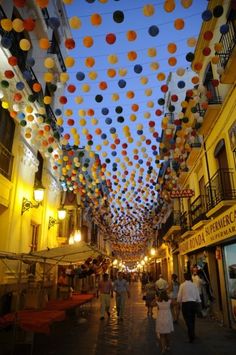 people walking down an alley way with many colorful balls hanging from the ceiling above them