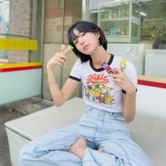 a woman sitting on a bench holding two toothbrushes in one hand and looking at the other