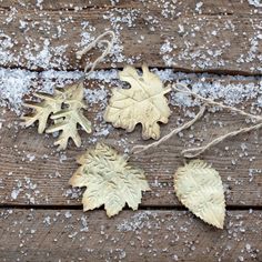 three leaf ornaments are hanging from string on a wooden surface with snow flakes all over them