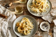 two plates of spaghetti with parmesan cheese and herbs next to glasses of wine