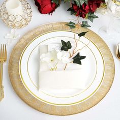 a white and gold plate topped with a piece of cake next to red flowers on top of a table